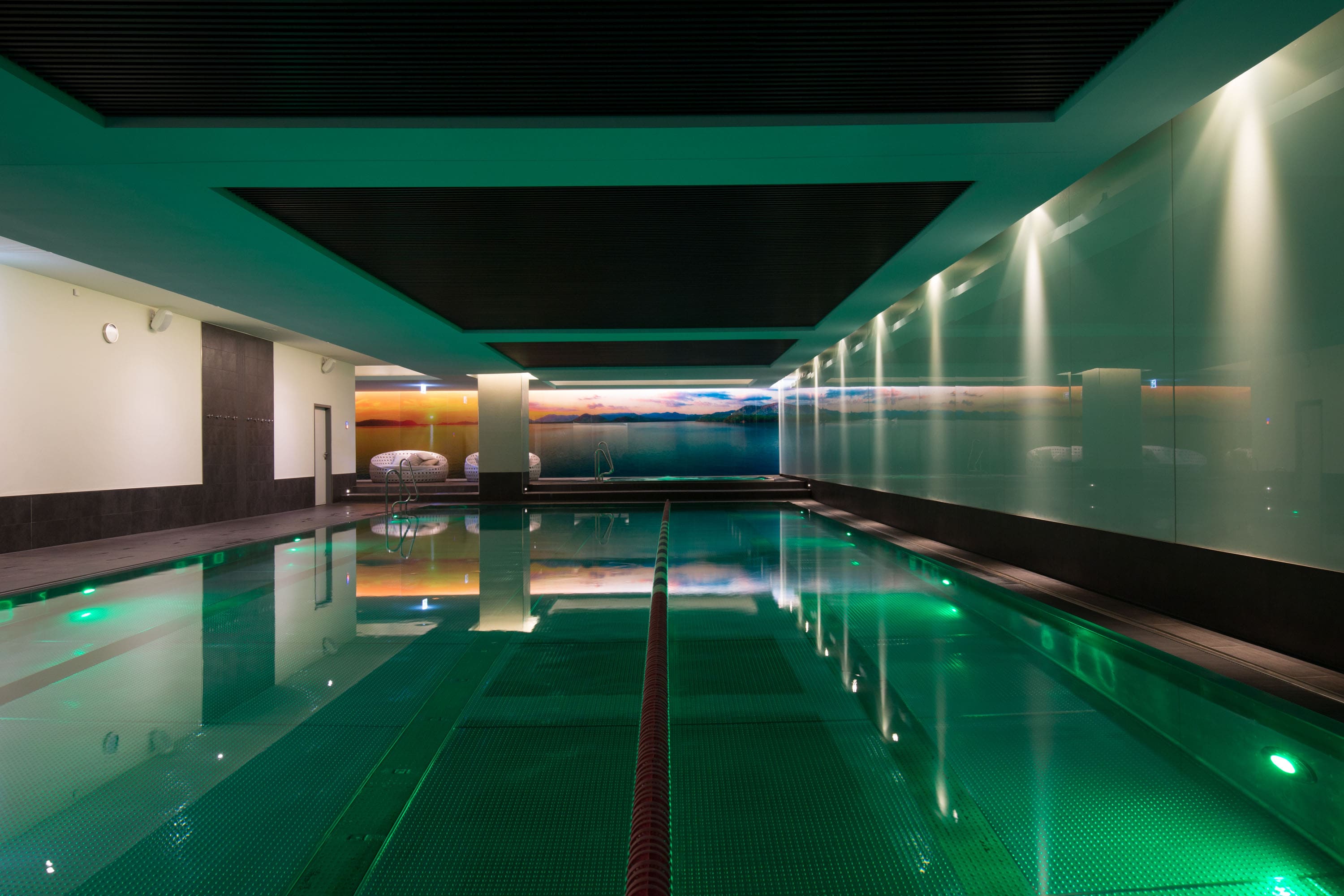 Luxuriöser Innenpool mit beruhigender grüner Beleuchtung und gehobenen Lounge-Sitzgelegenheiten in den Einrichtungen von Holmes Place.