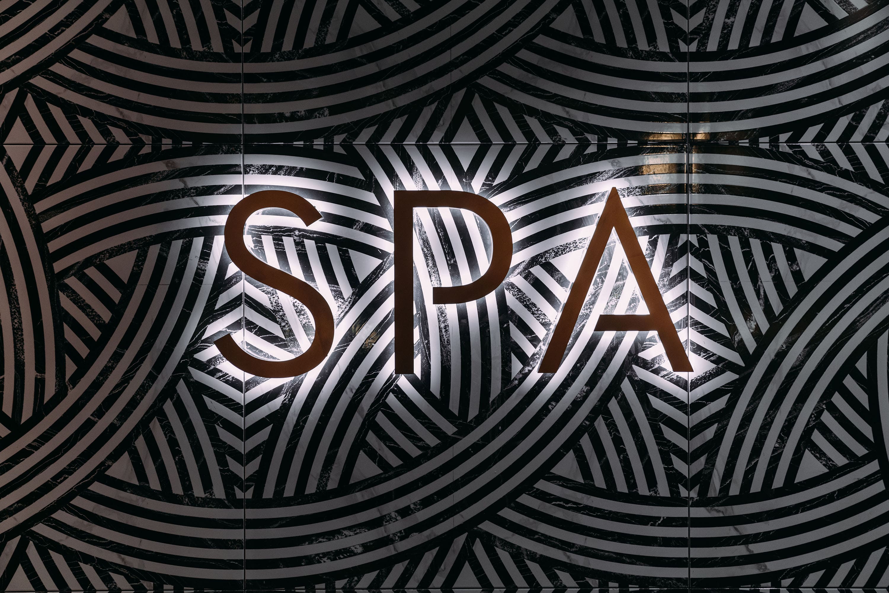 Holmes Place SPA-Schild auf einem markanten geometrisch gemusterten Hintergrund in kontrastierenden Braun- und Weißtönen.