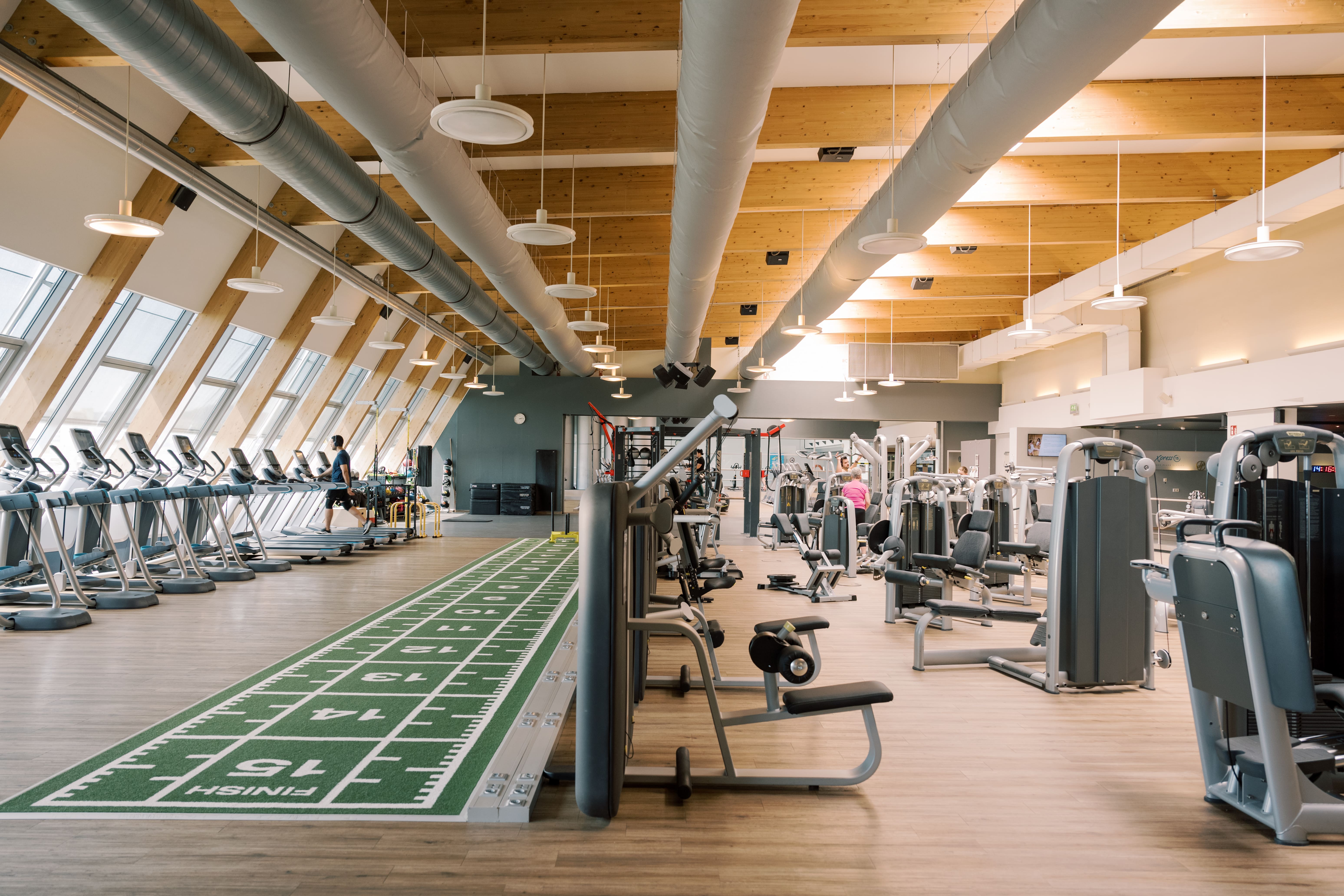 Das Fitnessstudio von Holmes Place besticht durch moderne Geräte auf einem Holzboden und einer grünen Laufbahn.