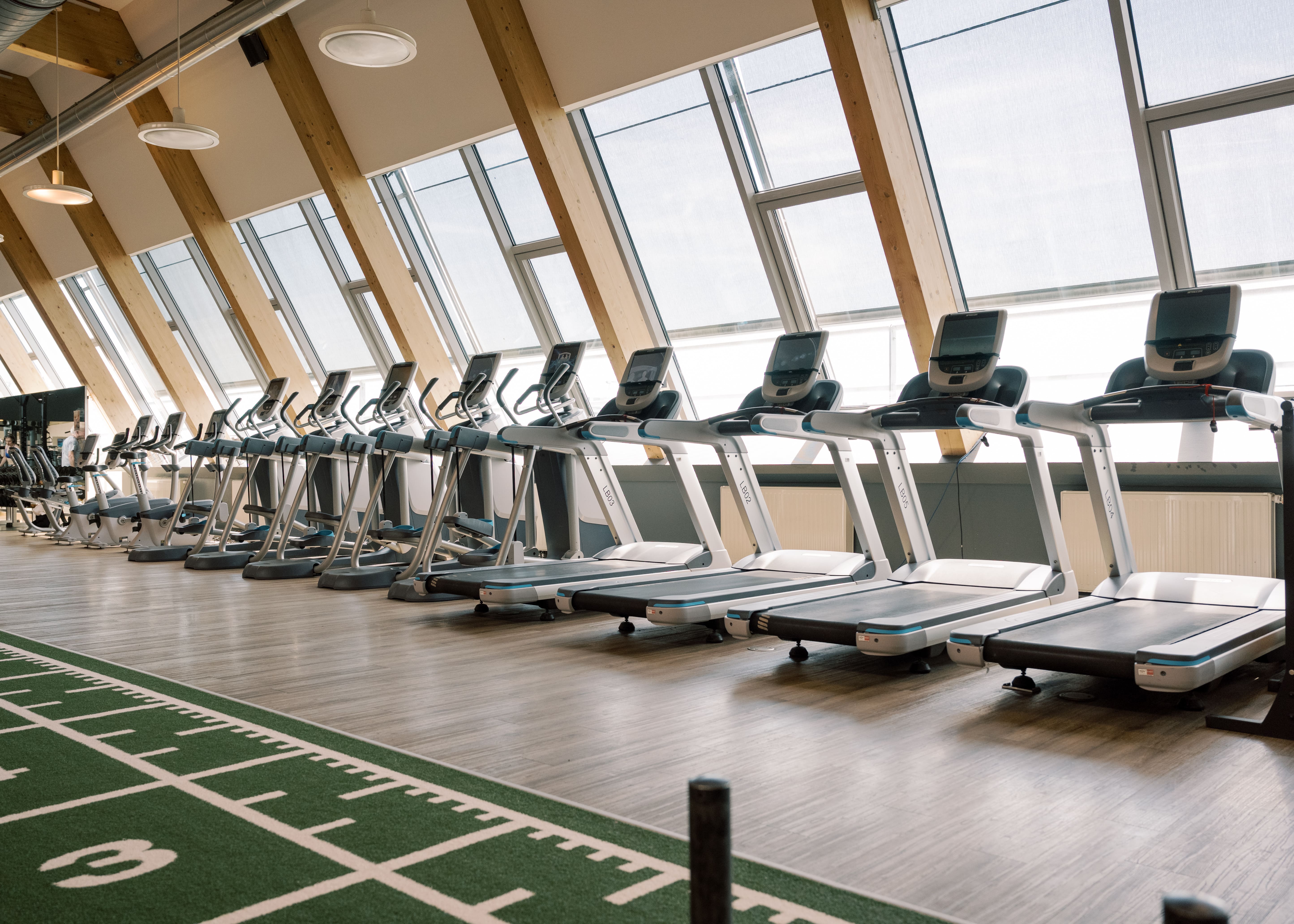 Die Laufbänder im Fitnessstudio Holmes Place verfügen über große Fenster und Holzakzente an den Wänden.