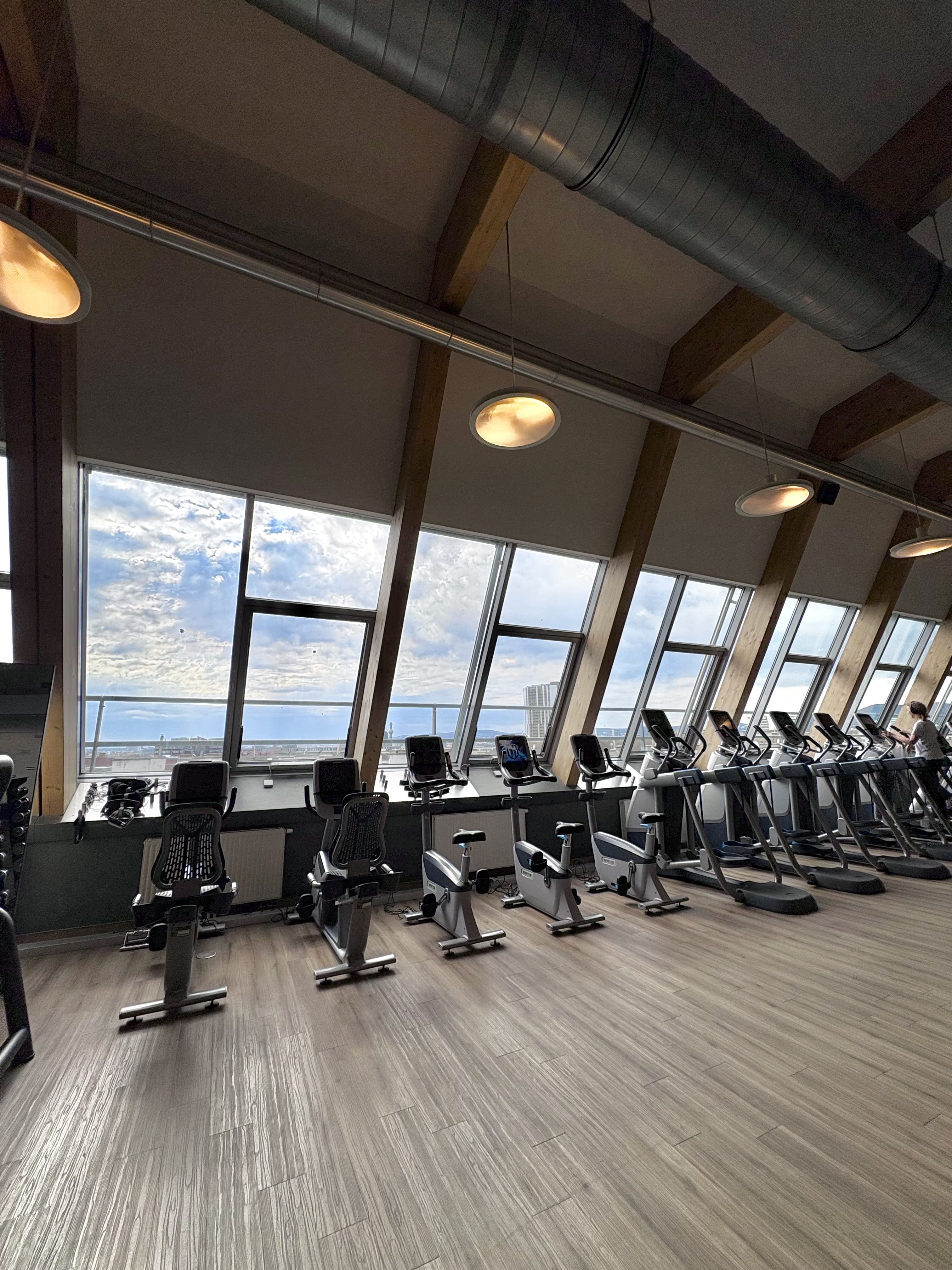 Das Fitnessstudio von Holmes Place verfügt über Heimtrainer und Laufbänder und bietet durch große Fenster einen Blick auf die Stadt.