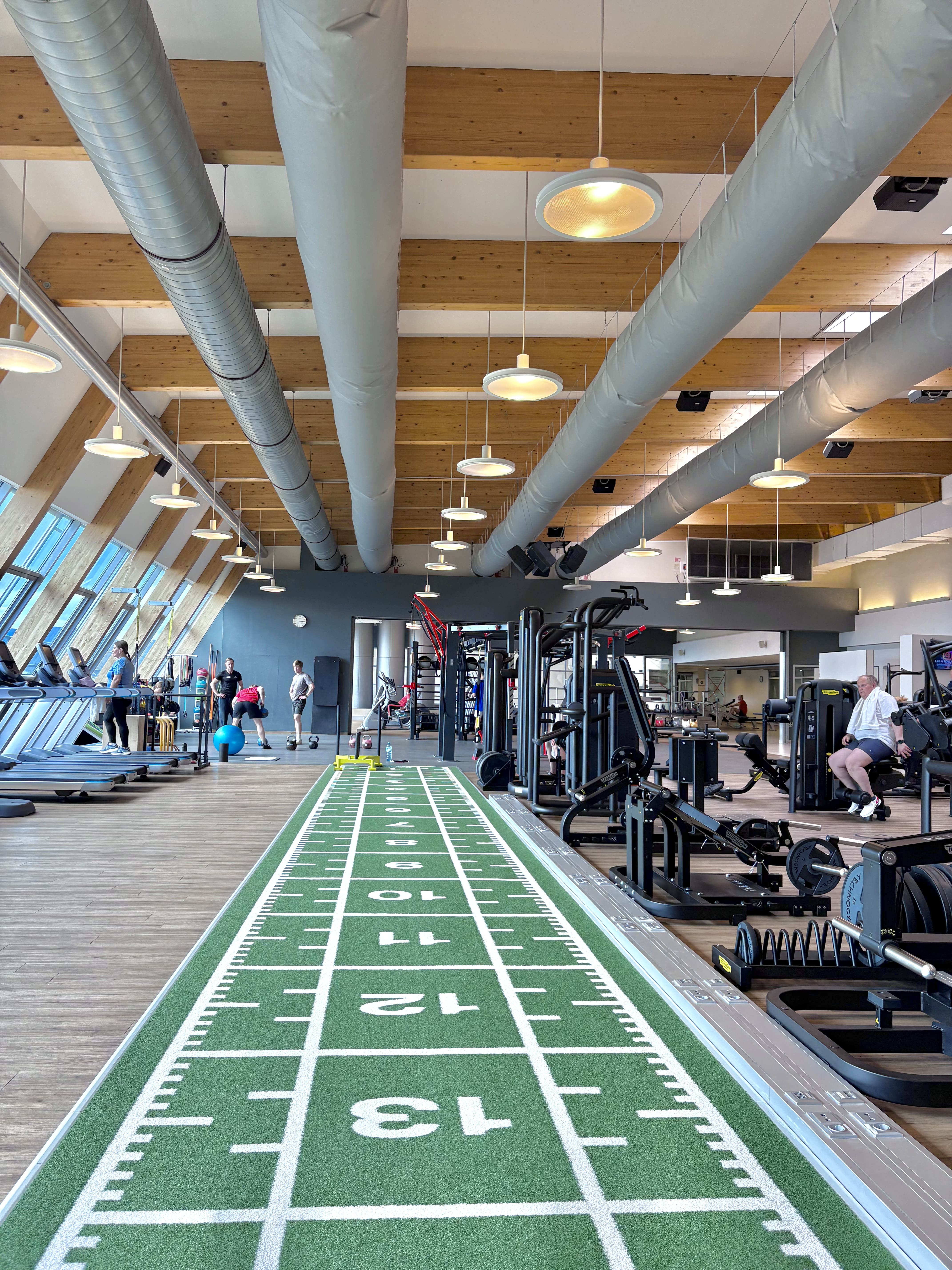 Innenansicht des Fitnessstudios von Holmes Place mit einer grünen Rasenbahn und Trainingsgeräten für das Workout-Training.