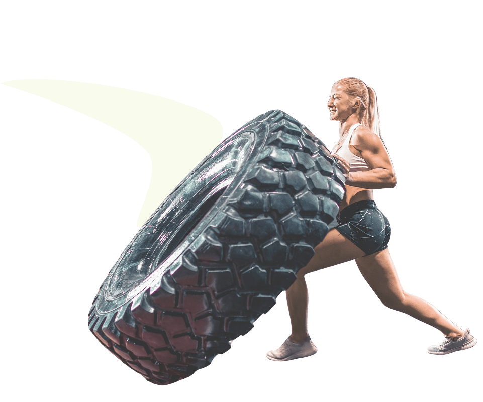 Athletic woman in workout clothes flipping a large tire during fitness training.