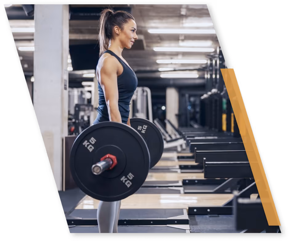 Woman lifting two 5 kg barbells in a gym with workout equipment in the background.