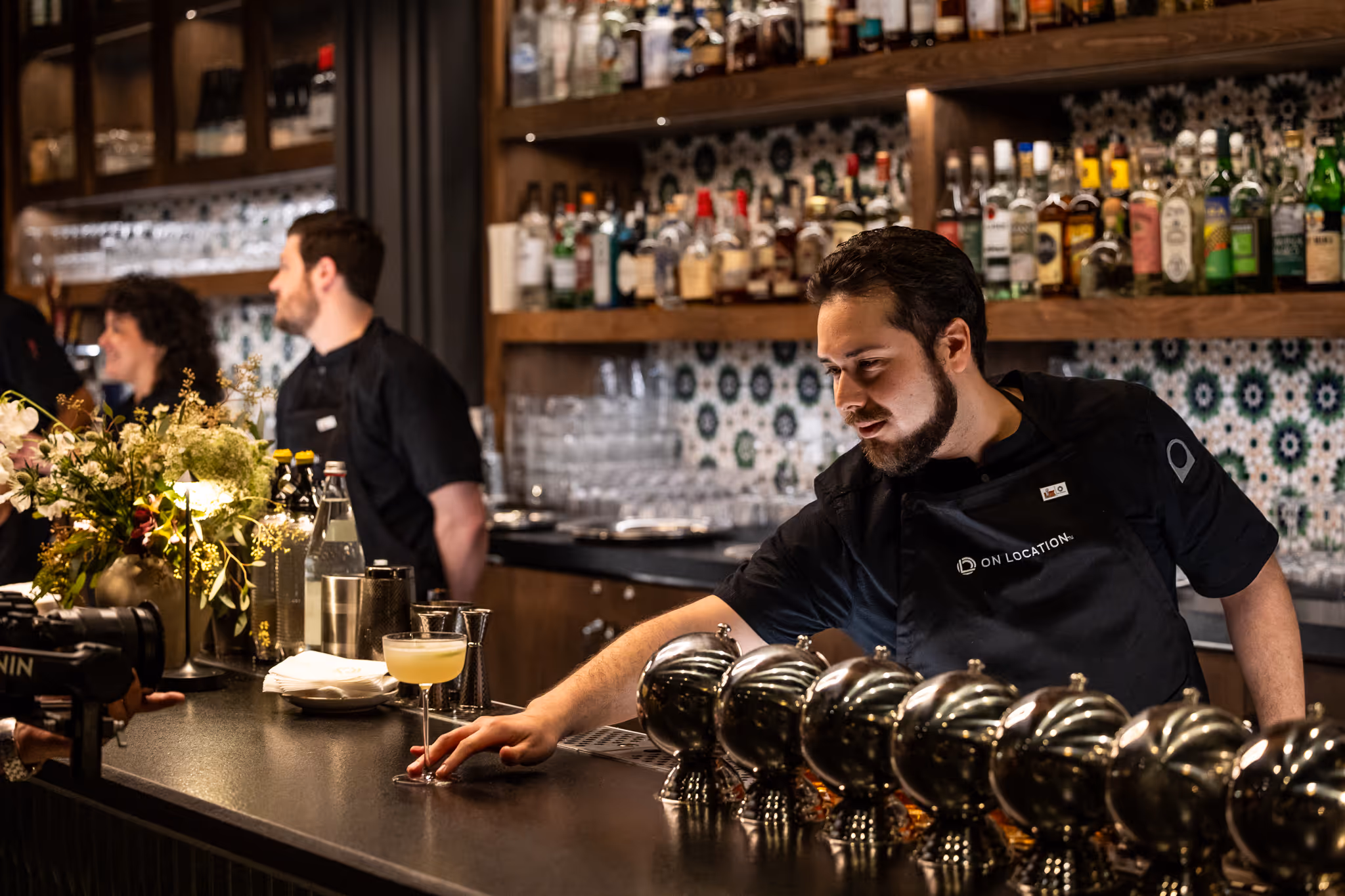 Bartender preparing cocktail at bar with extensive liquor collection