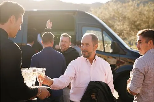 Group of men in business casual clothing toasting with champagne near van