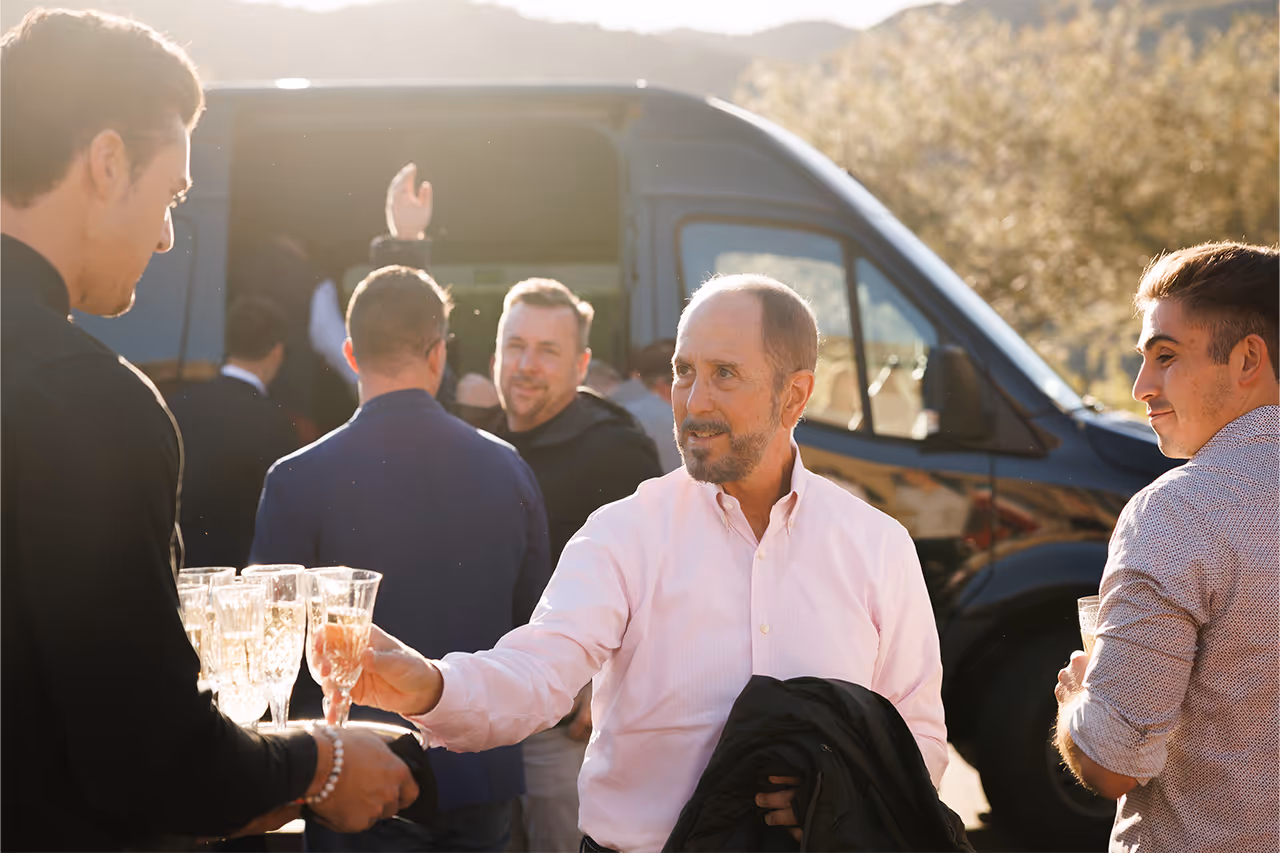 Group of men in business casual clothing toasting with champagne near van