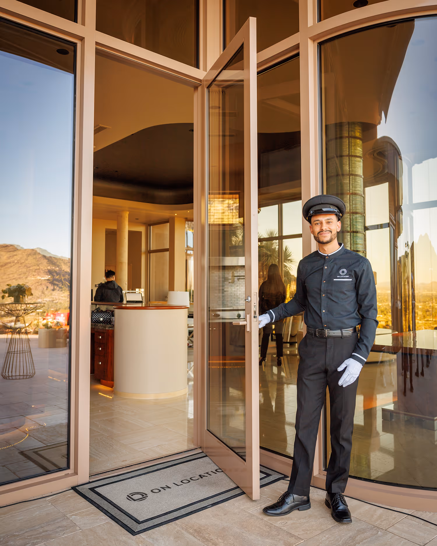 Doorman in uniform standing at entrance of modern hotel with mountain view