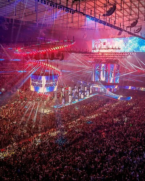 Large wrestling arena with colorful lights and packed crowd during event