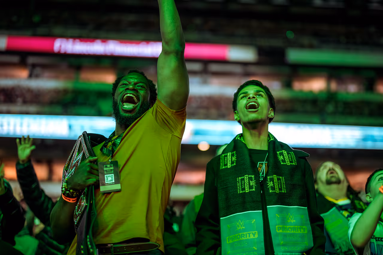 Fans cheering with excitement at a WWE event, bathed in green light