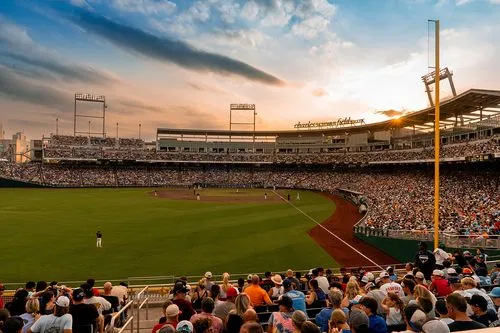Packed baseball stadium at sunset with players on the field