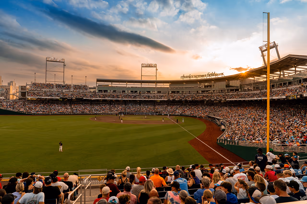 Packed baseball stadium at sunset with players on the field