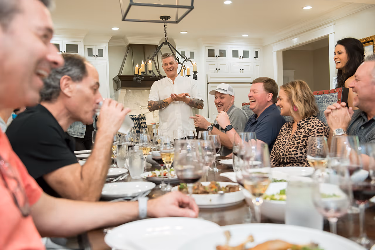Chef entertains laughing group during dinner party in elegant kitchen