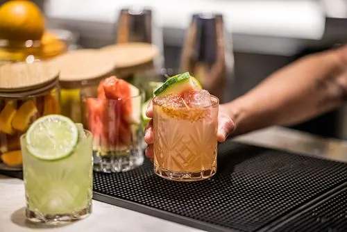 Two craft cocktails with lime garnish on a bar with bartending tools
