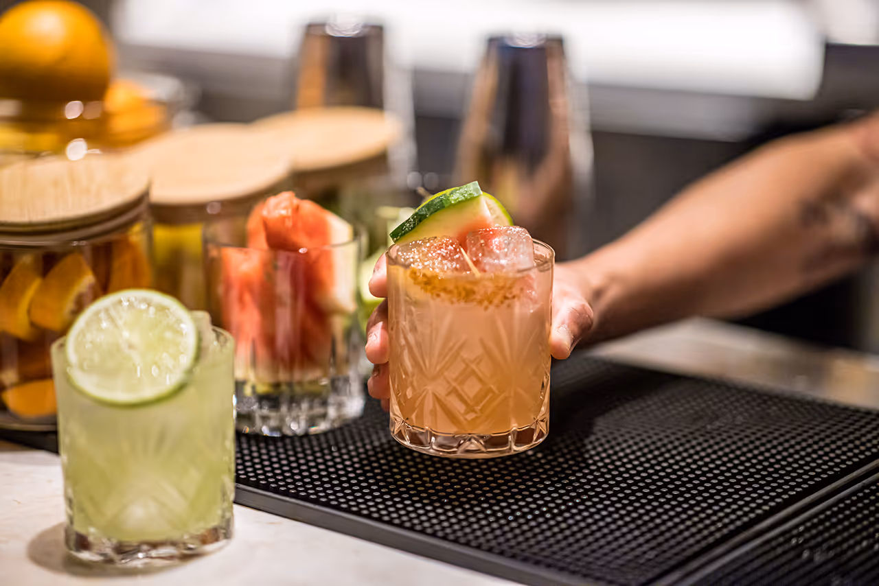 Two craft cocktails with lime garnish on a bar with bartending tools