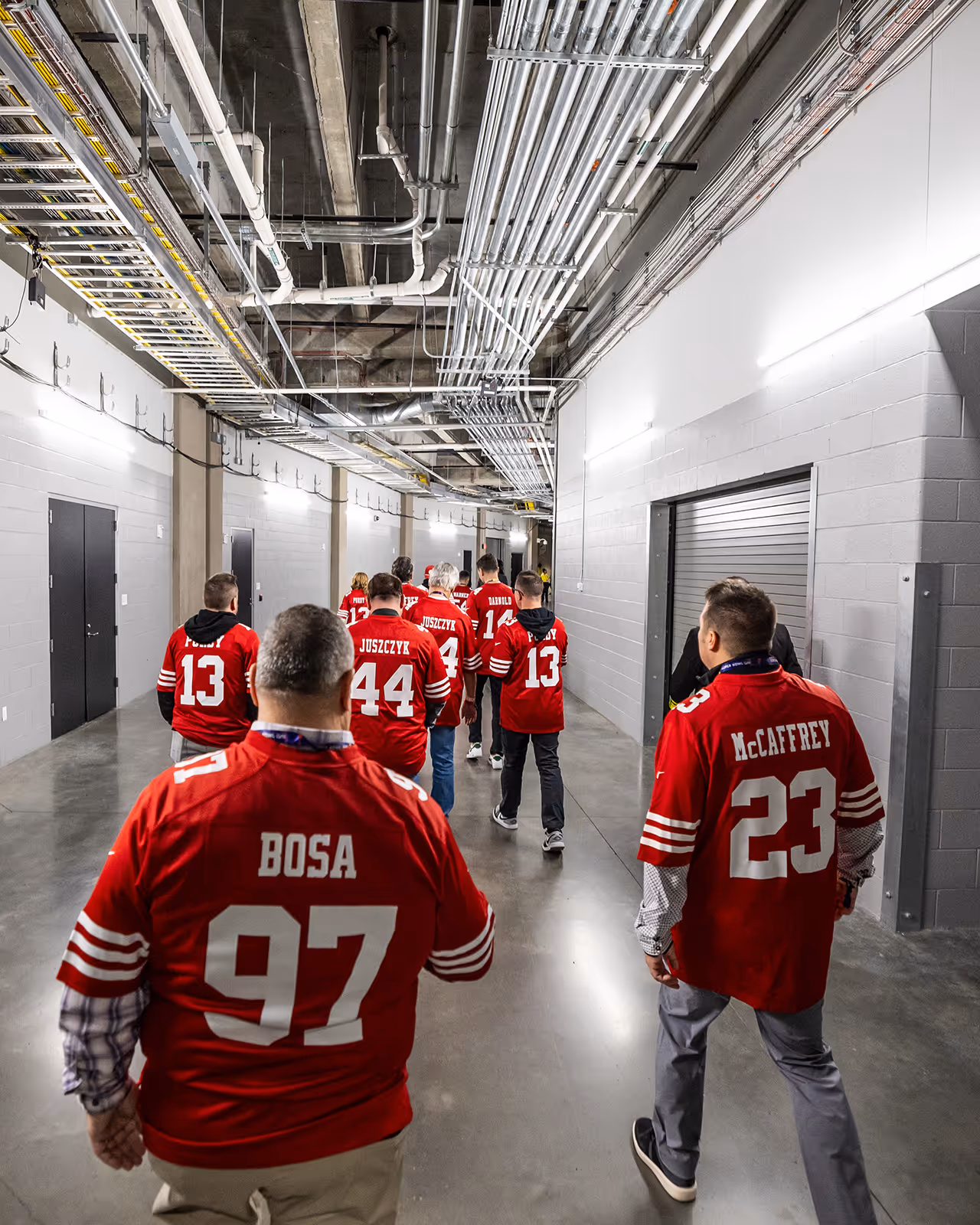 Football players in red jerseys walking down industrial-looking hallway