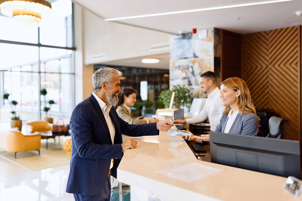 Business professional paying at hotel reception desk with smiling staff
