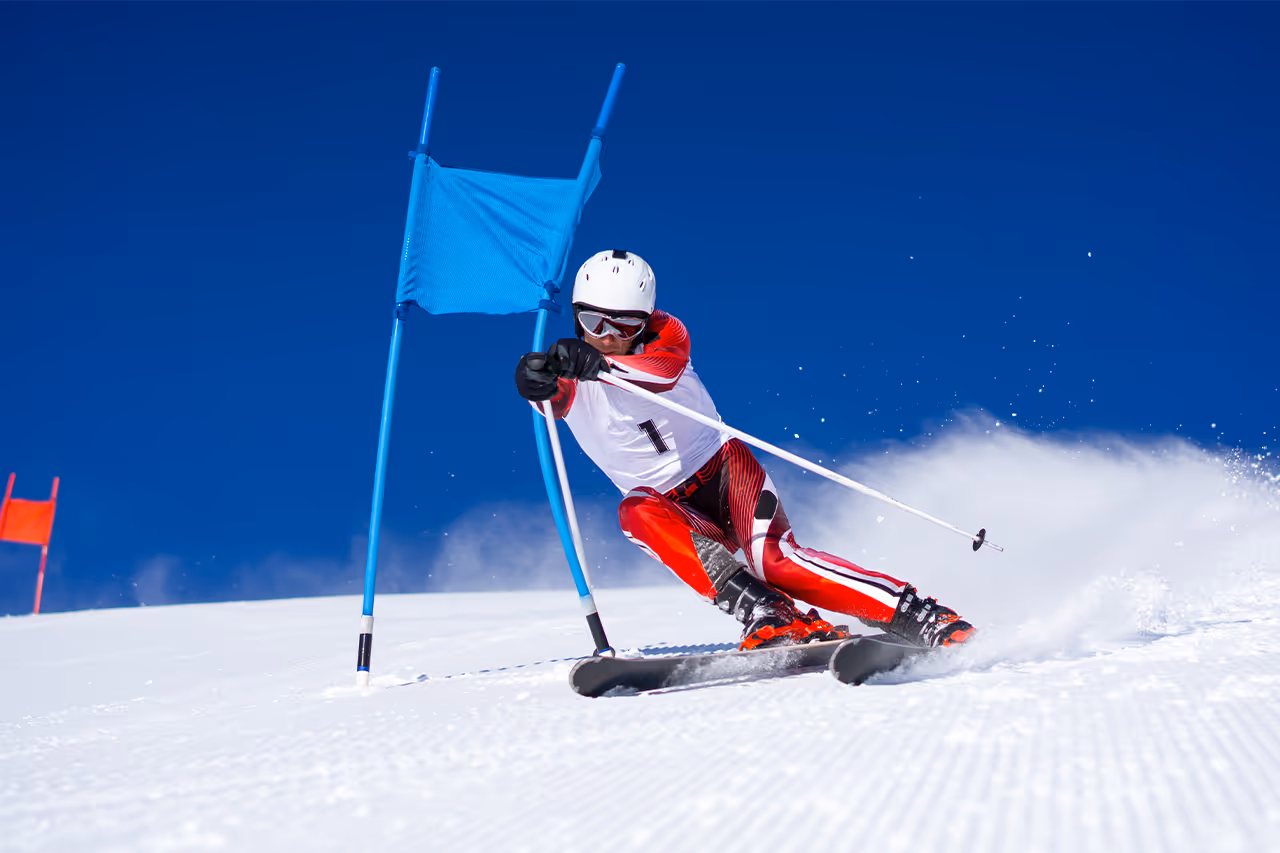 Skier in red and white racing down slalom course against blue sky