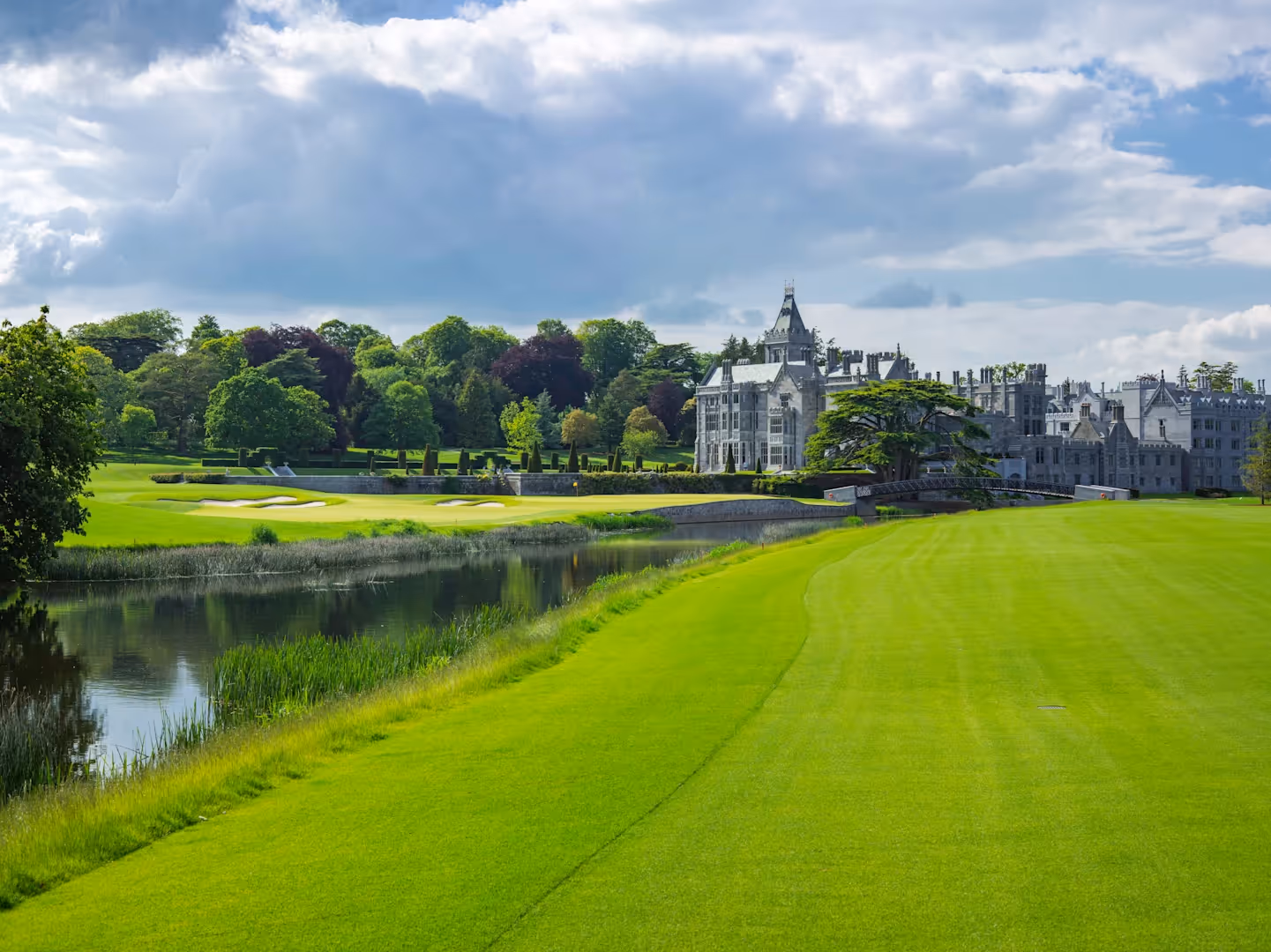 Elegant castle with manicured golf course and lake under cloudy sky