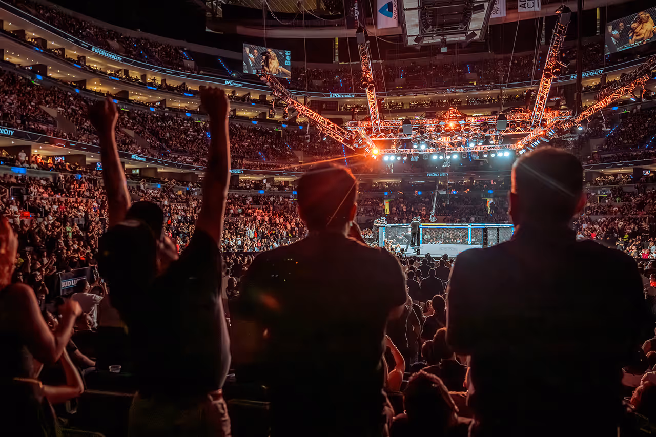 Packed UFC arena with fighting cage and excited crowd from behind