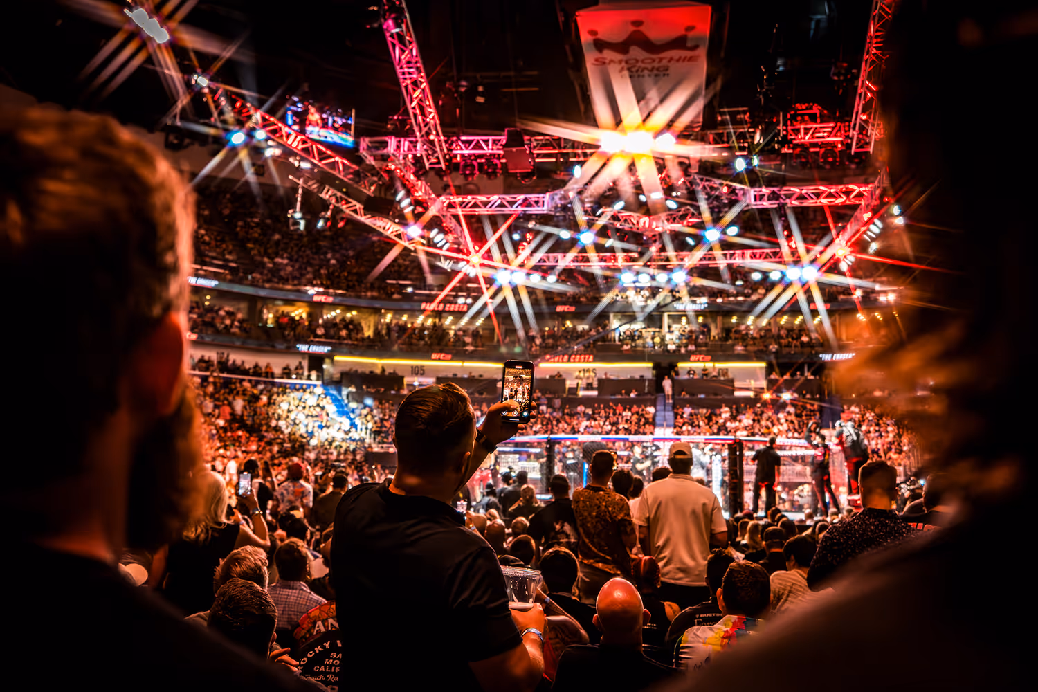 Packed arena with bright lights during a UFC event, audience watching fight