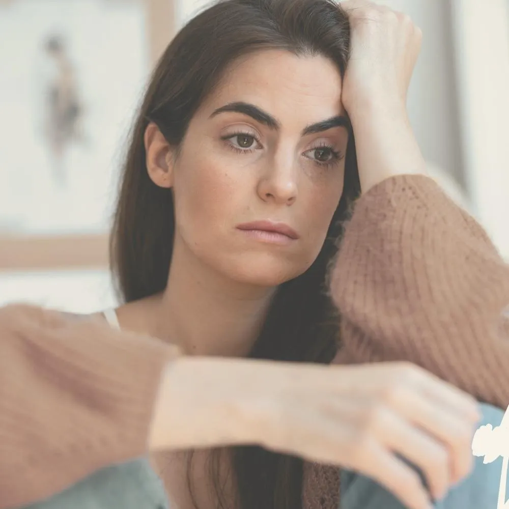 Nachdenkliche Frau stützt ihren Kopf auf die Hand, wirkt müde oder besorgt.