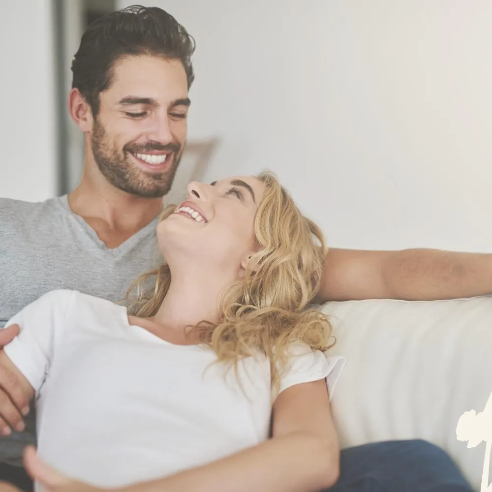 Ein lächelndes Paar sitzt auf einem Sofa, die Frau lehnt sich glücklich an den Mann.