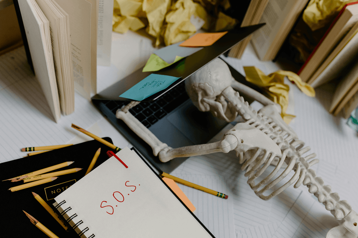 A skeleton dying on a computer with a SOS sign on his notebook