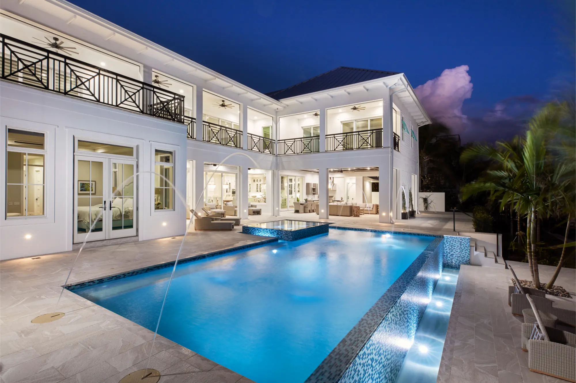 Large two-story house with illuminated swimming pool and deck at dusk.