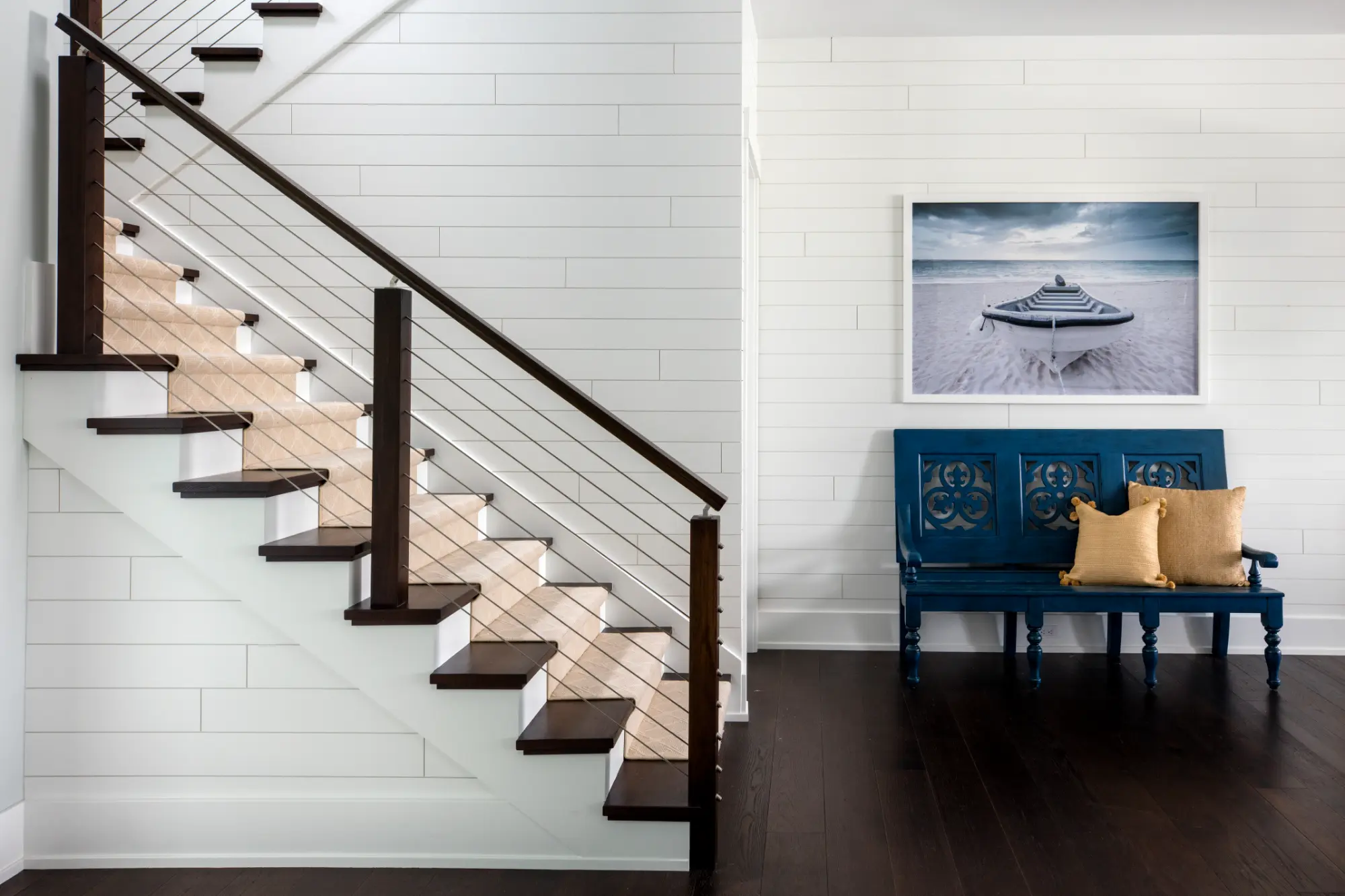 A staircase with dark railings next to a blue bench with cushions and a framed boat picture.