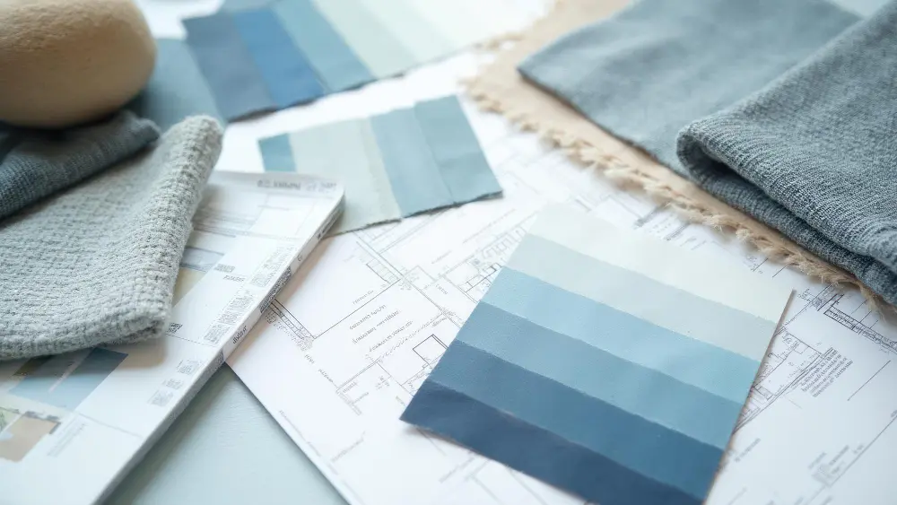 Various blue fabric swatches and a blueprint lay on a table, suggesting an interior design project.