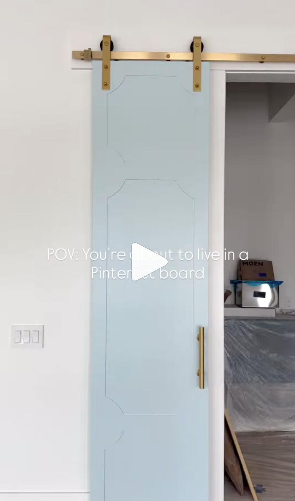 Light blue sliding barn door with gold hardware partially open, revealing a room with covered furniture and boxes.