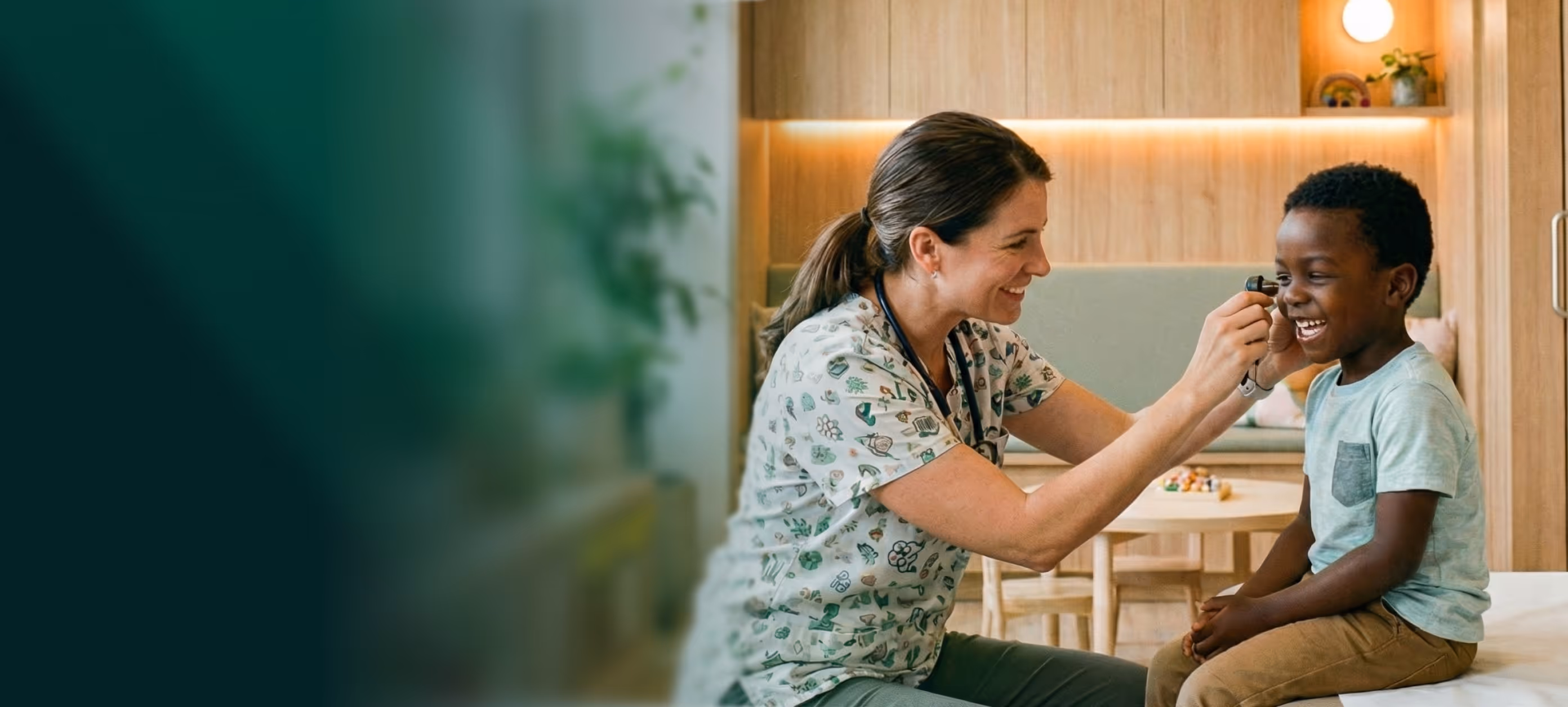 Female healthcare professional smiling while examining a laughing boy's ear with a medical otoscope in a brightly lit room.