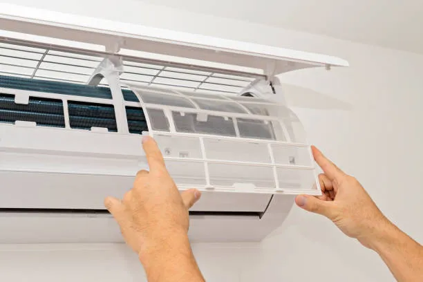 Hands opening and cleaning air conditioning filter on wall-mounted unit