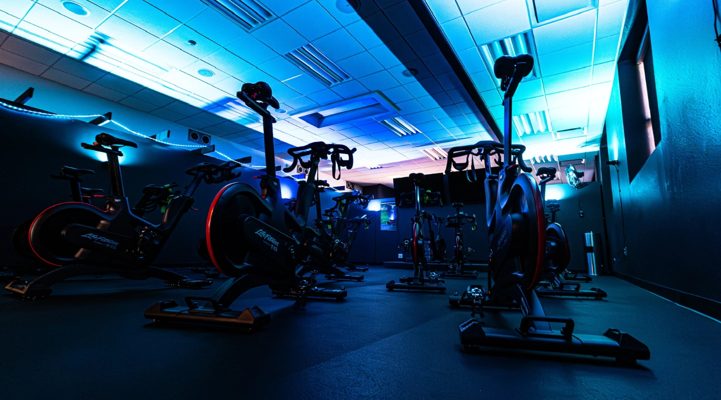 A dimly lit spin studio featuring rows of stationary bikes illuminated with vibrant blue and red lighting.