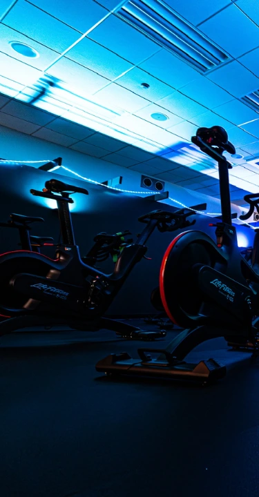 A dimly lit spin studio featuring rows of stationary bikes illuminated with vibrant blue and red lighting.
