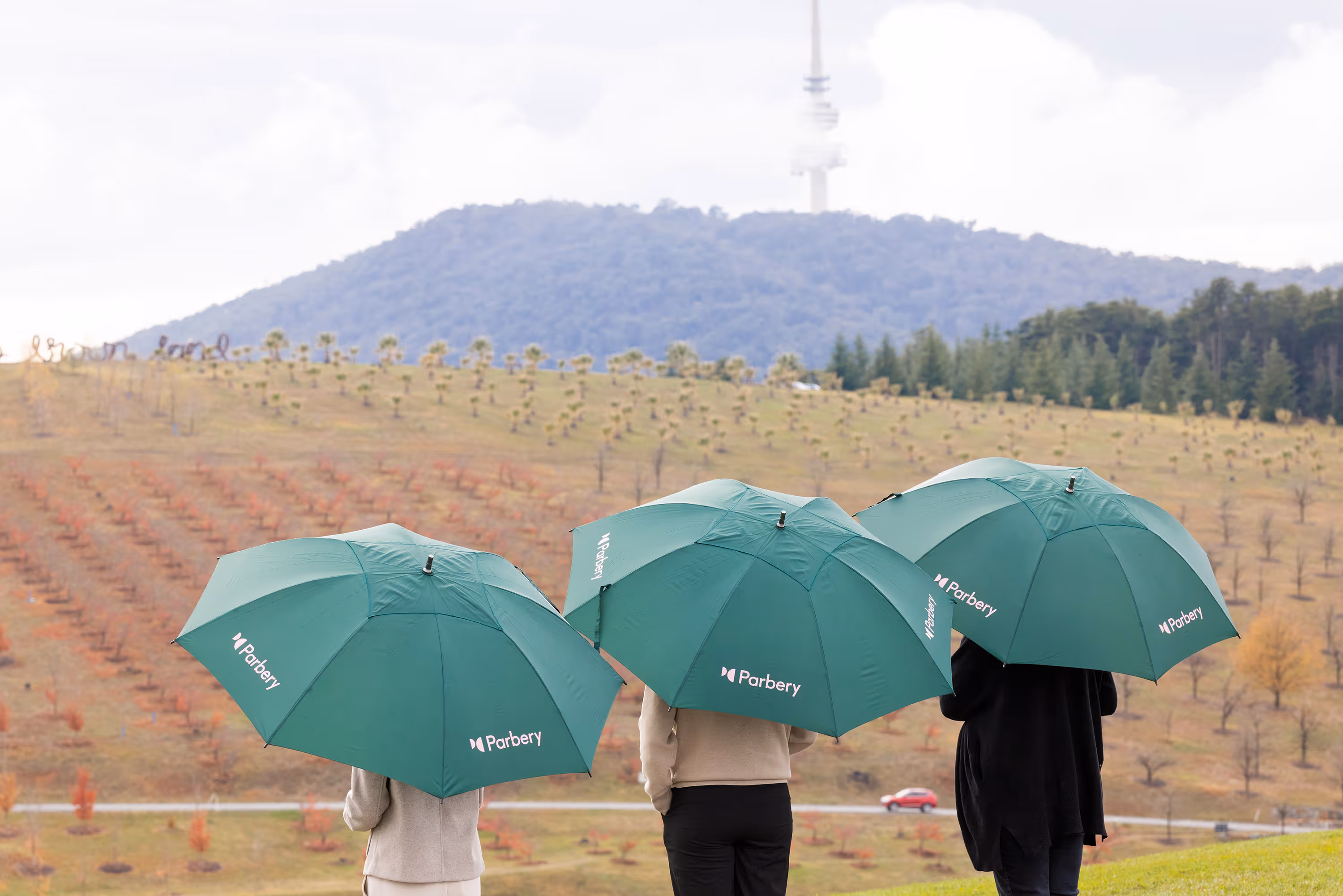 3 Parbery employees holding green Parbery branded umbrellas.