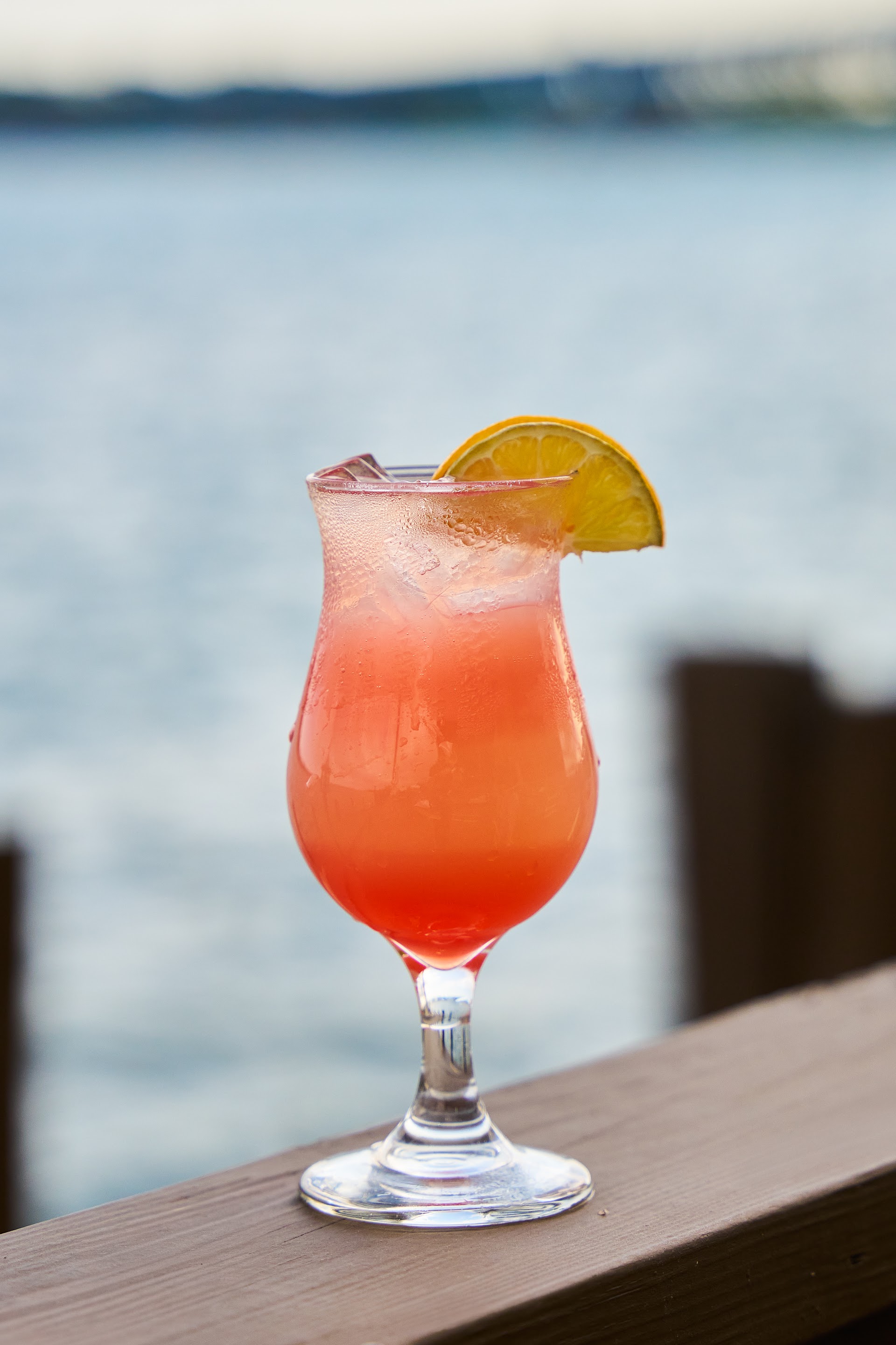 A pink cocktail on the patio railing at Bella Vista with the river and bridge behind