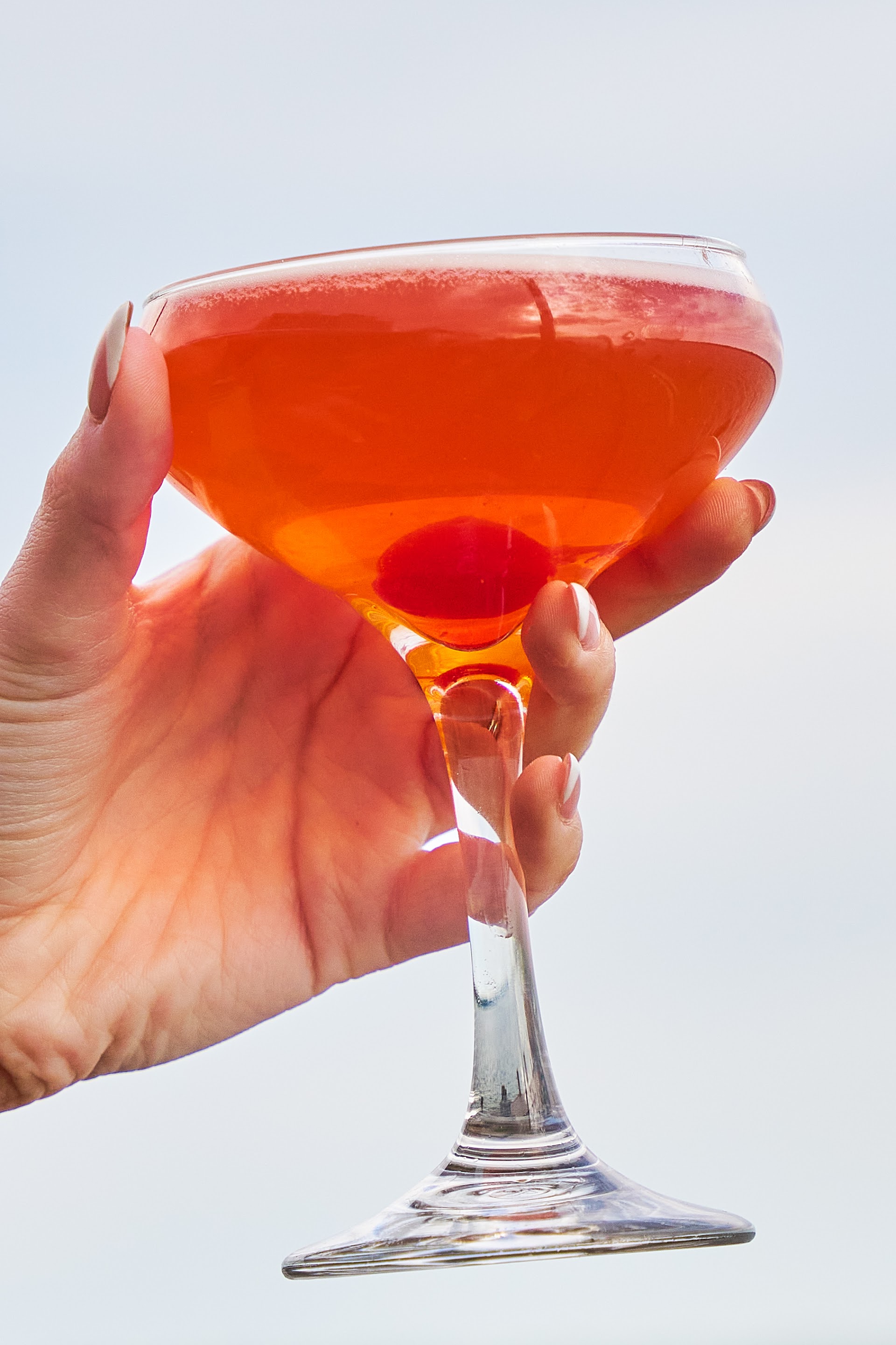 A hand raising a coupe cocktail against the evening sky at Bella Vista