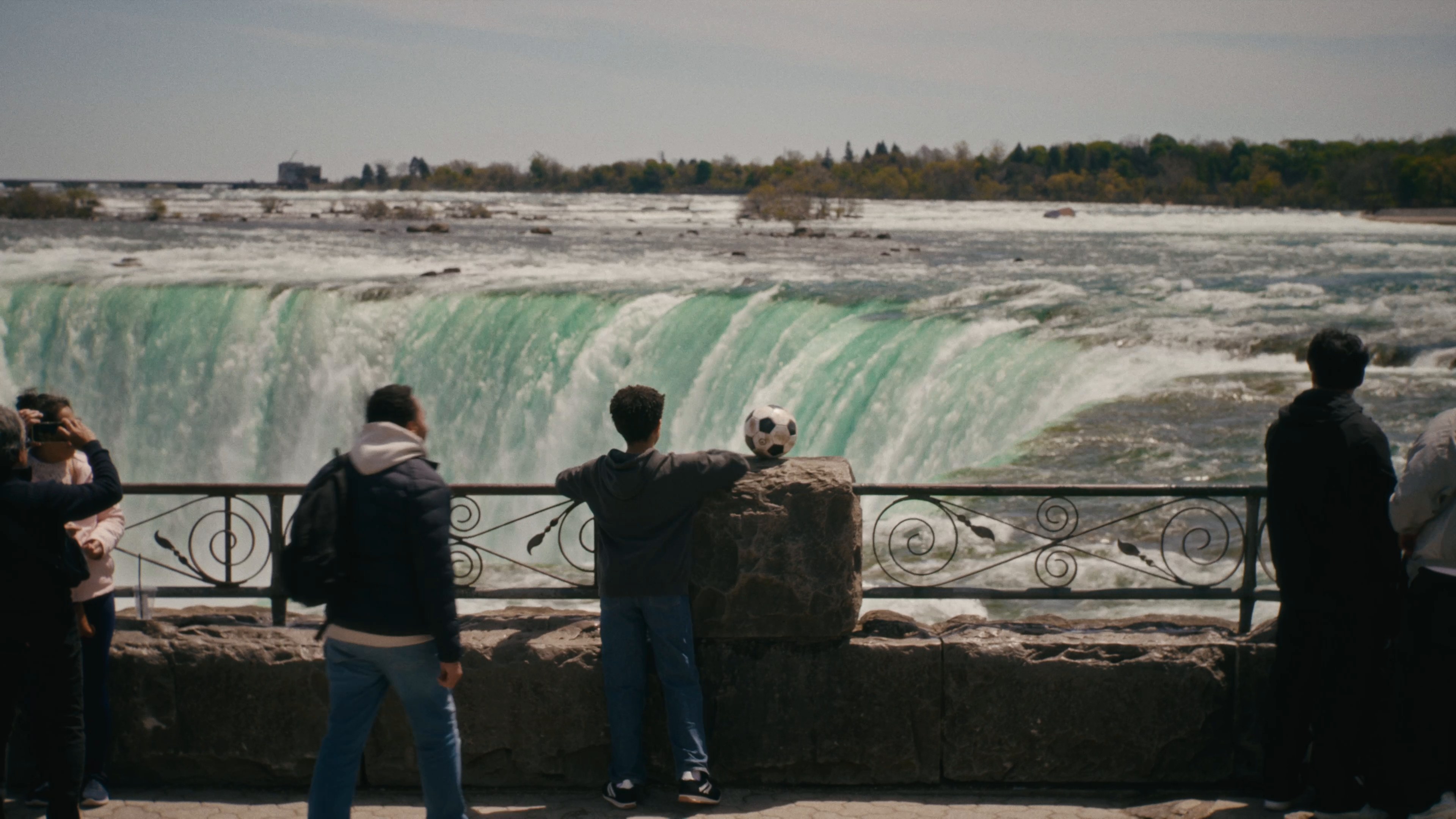 A boy holds his soccer ball at the railing above the brink of the Horseshoe Falls, from the Where the World Comes to Play film