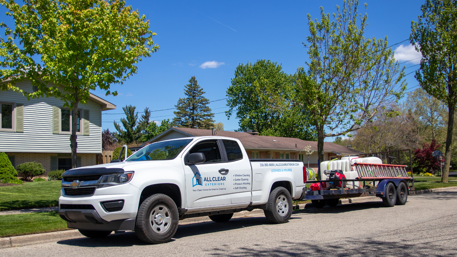 White All Clear Exteriors truck parked on a street towing a trailer with cleaning equipment under blue sky.