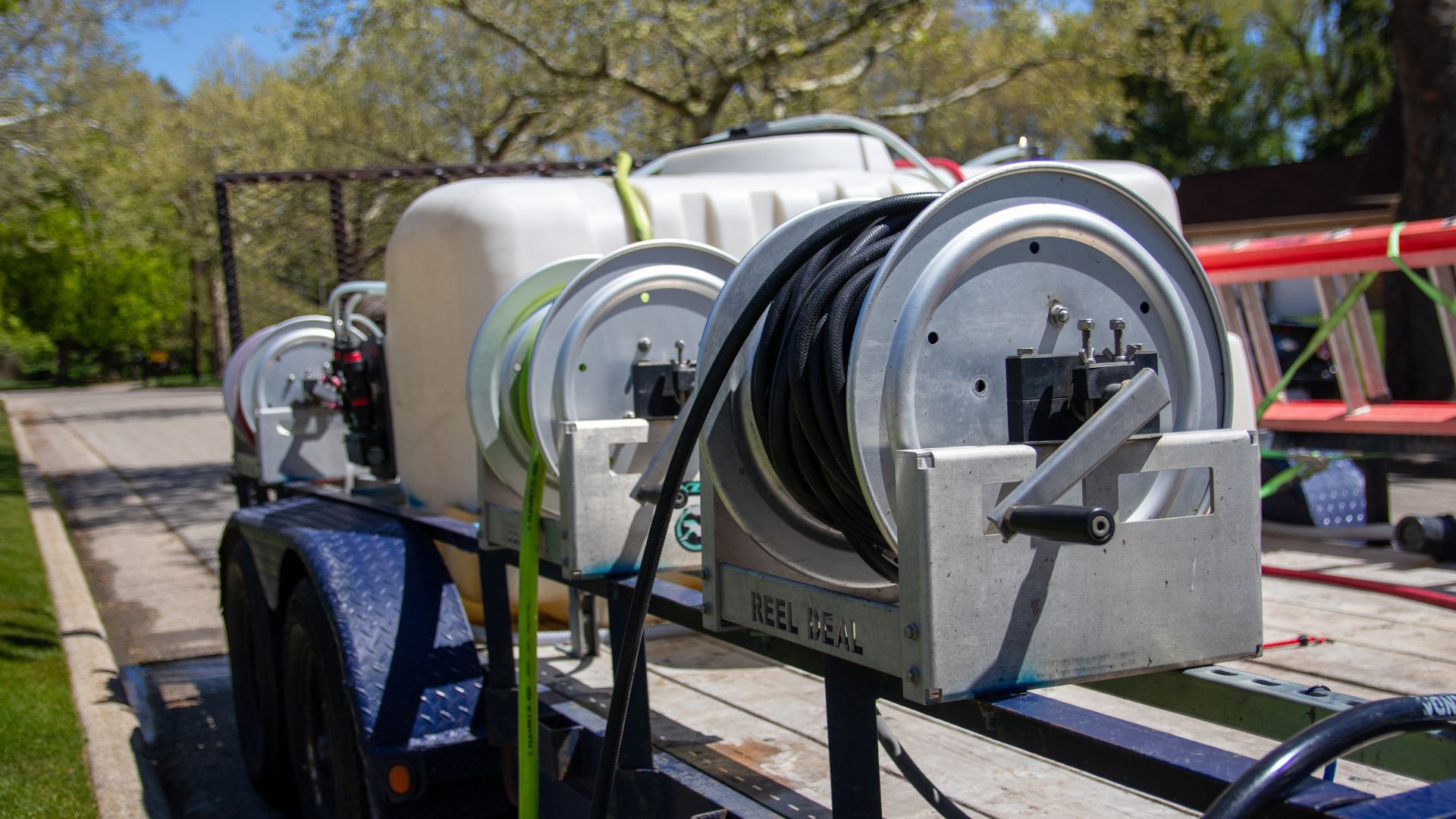 Trailer with large white tank and hose reels for spraying or cleaning on a sunny day.
