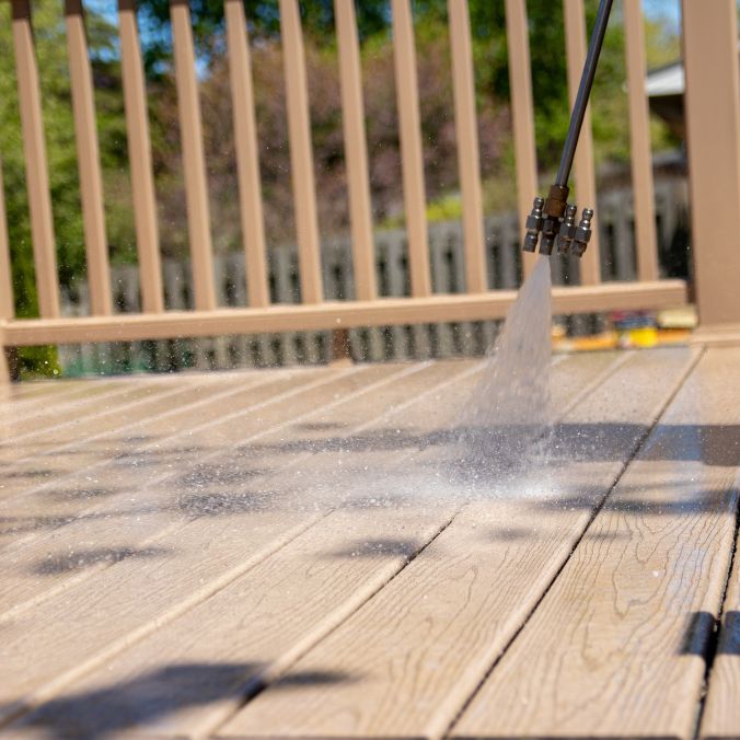 Pressure washer spraying water on a wooden deck outdoors with railing and blurred background.