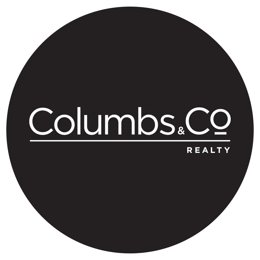 A logo for Columbs & Co. Realty. The text is in a thin, white, sans-serif font. The words "Columbs & Co" are in a larger font with a horizontal line underneath. The word "REALTY" is in a smaller font below the line. The entire text is centered within a solid black circle.