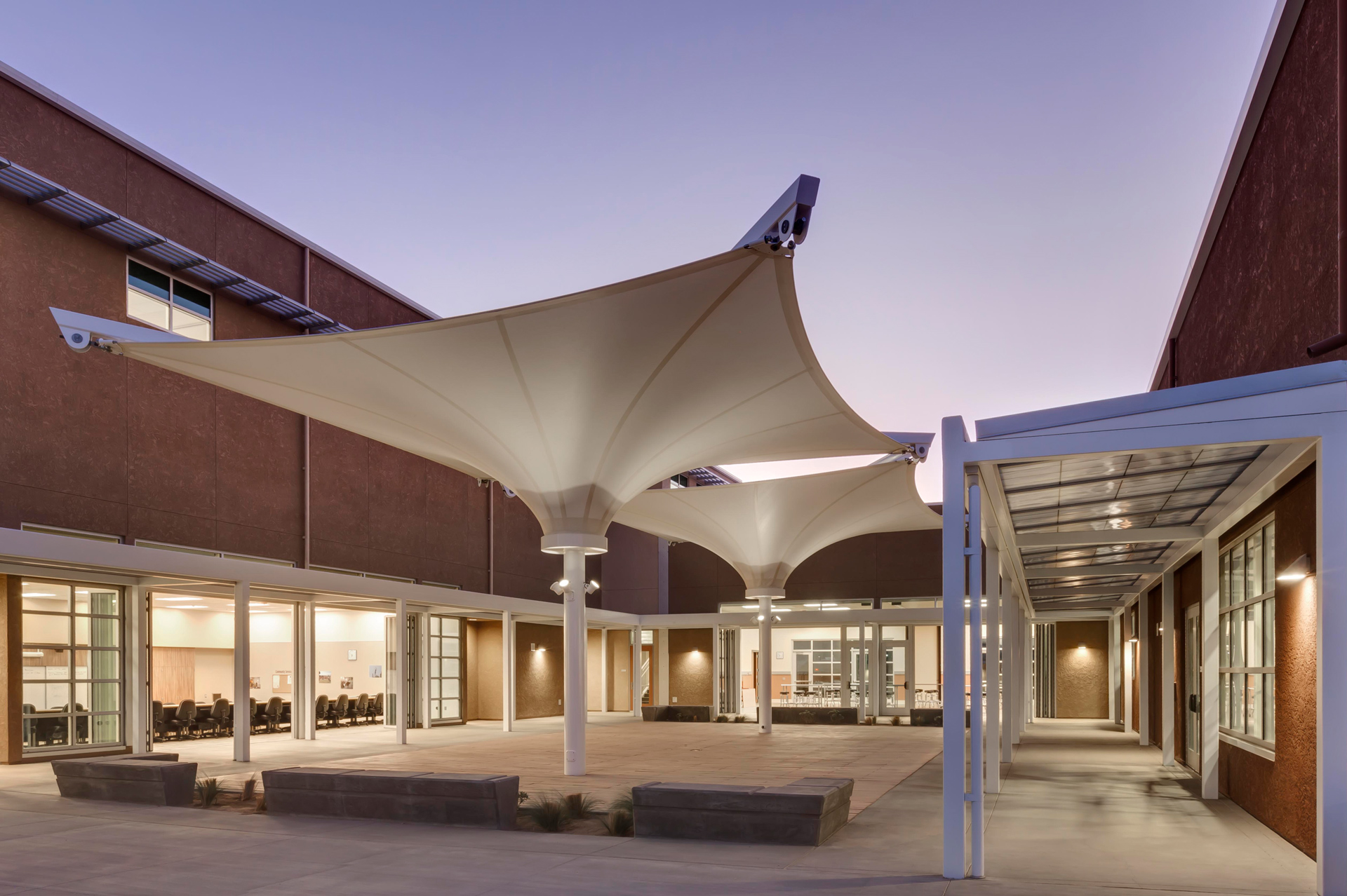 Modern courtyard with tensile fabric canopy structures and integrated exterior lighting at dusk, Newport Beach campus.