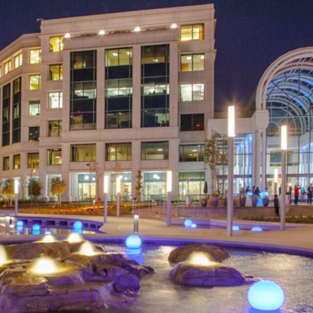 Close-up of Water Garden fountain with glowing lights in front of modern office building at night