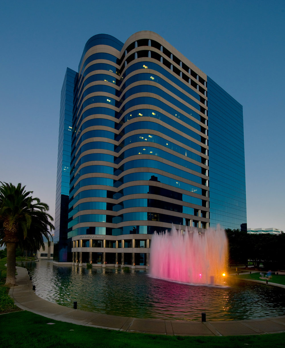 Modern high-rise office tower with curved blue glass façade and palm trees in front under a clear sky.