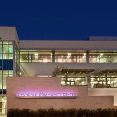 Exterior night view of the Lawndale Community Center, featuring modern glass architecture and illuminated signage.