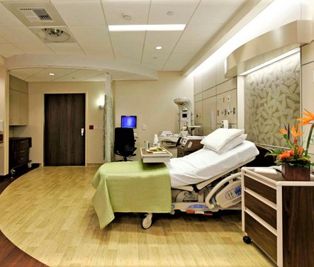 Hospital patient room with bed, seating area, and large window view
