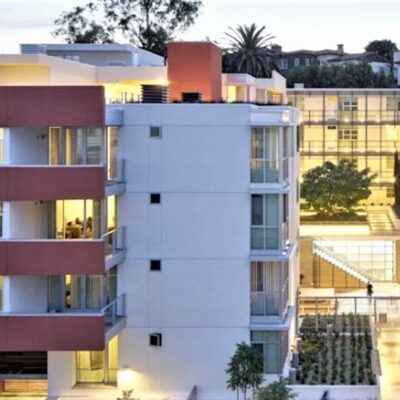 Modern white and red apartment-style housing complex with large windows and balconies, lit warmly in the evening.